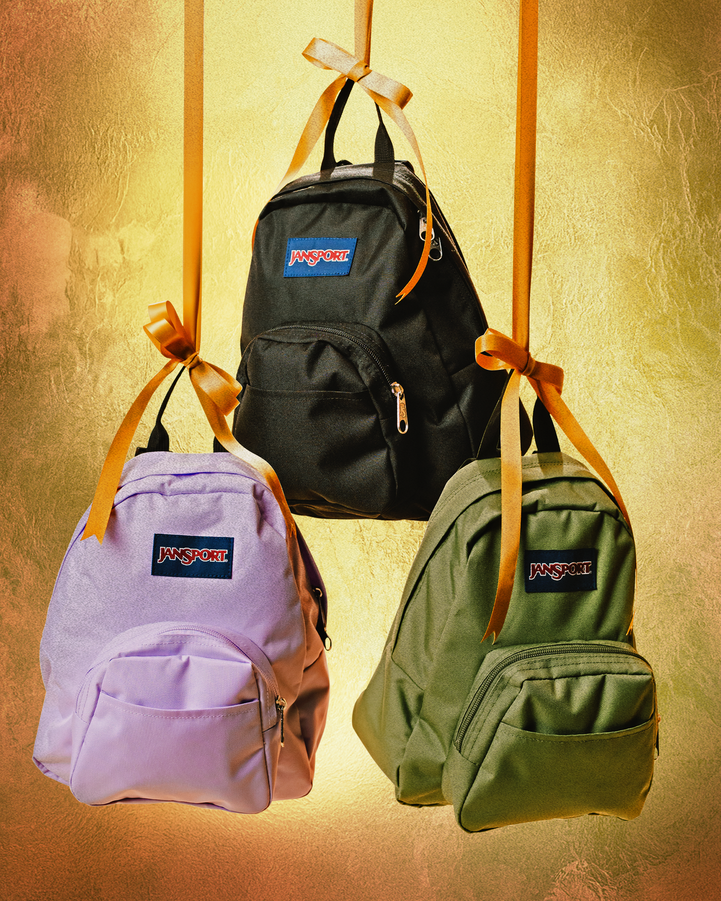 Three jansport half pint backpacks on a gold background tied up with orange ribbon